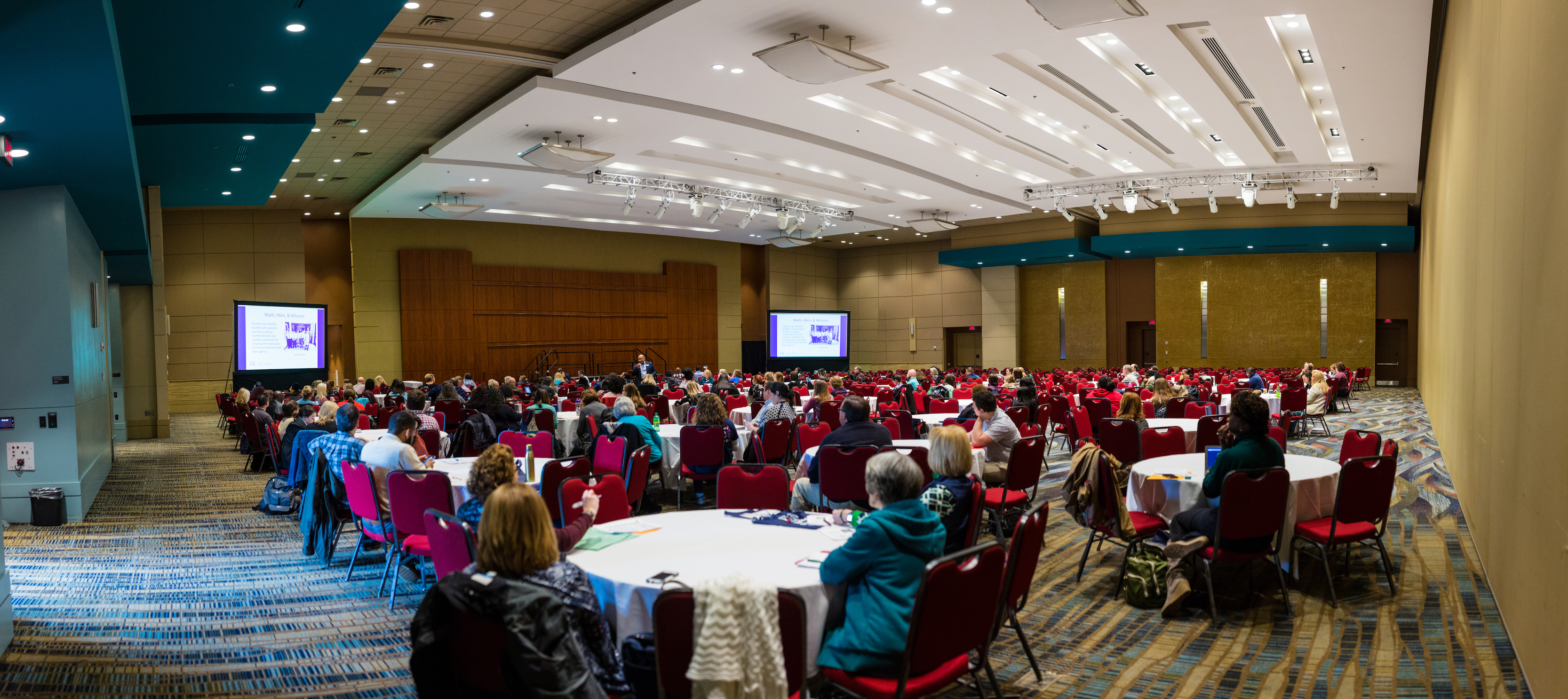 Clusters of round tables facing a podium where a speaker addresses the crowd